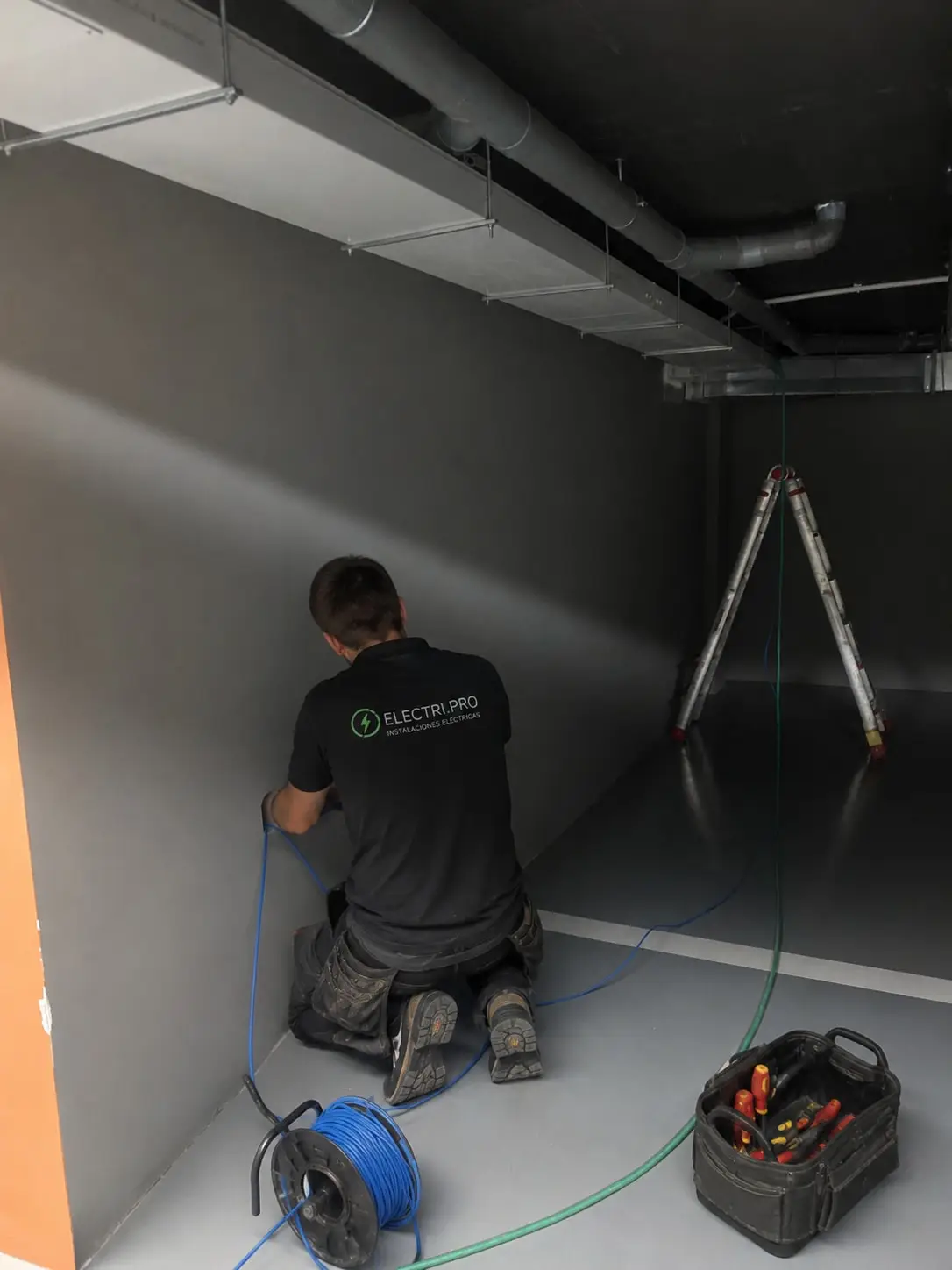 Electrician pulling cable in an underground garage, with a ladder, cable drum and tool bag