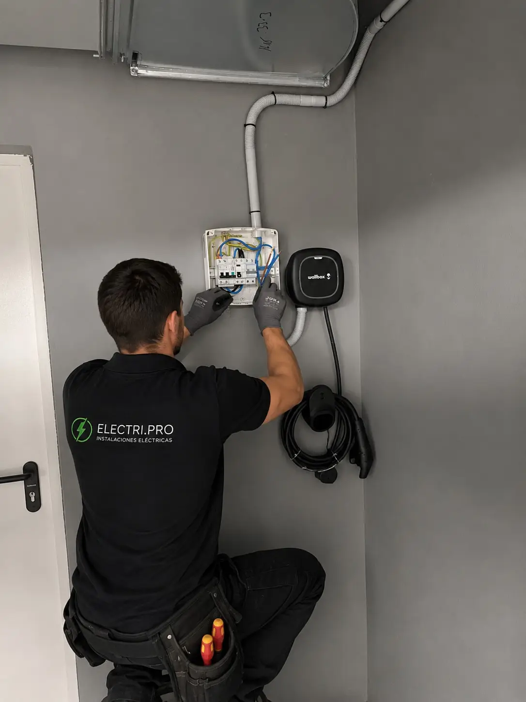 Electrician wiring the surface-mounted protection box next to the already-mounted charger