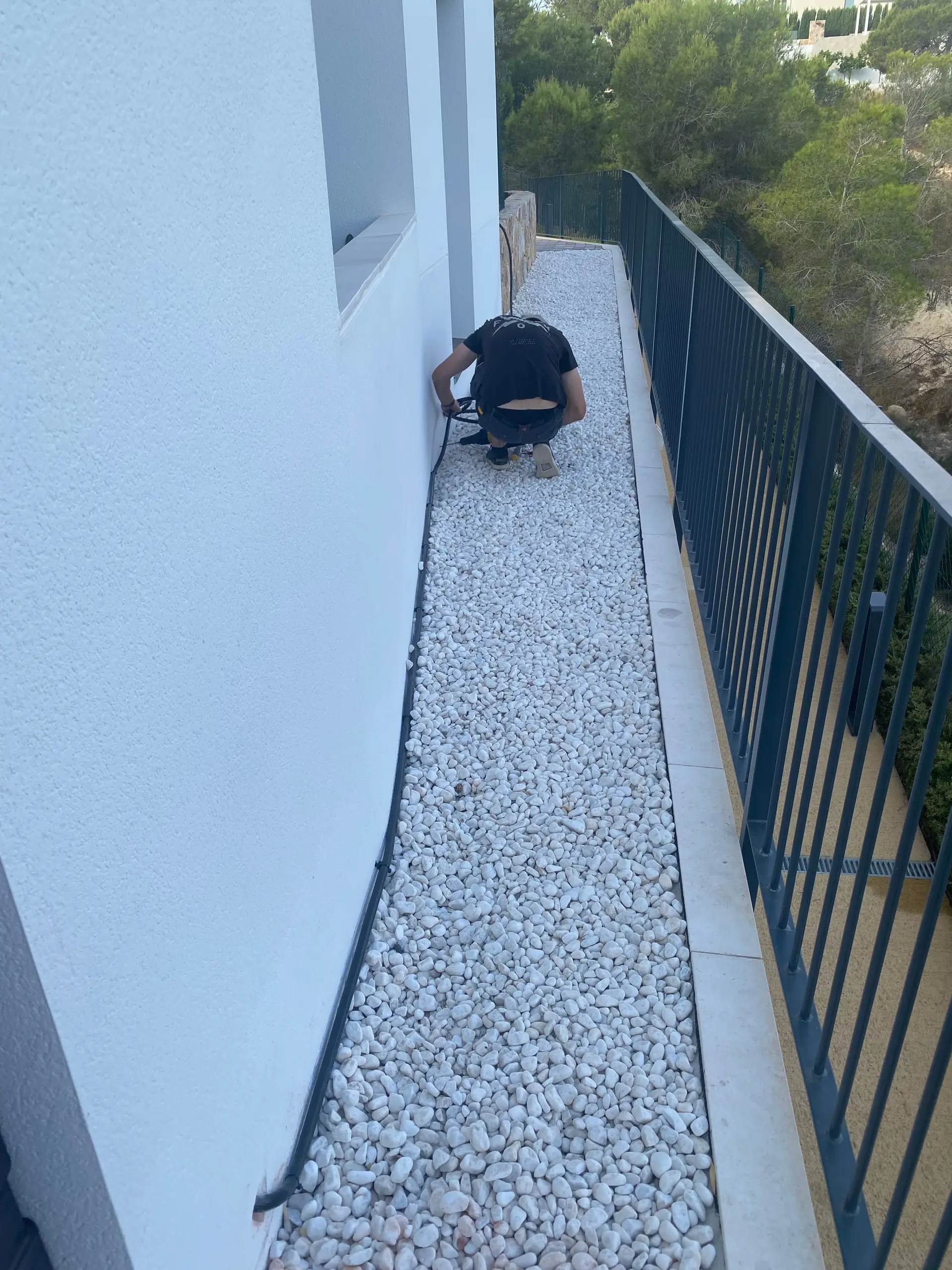 Electrician crouched running cable along a strip of white gravel between the wall and the railing