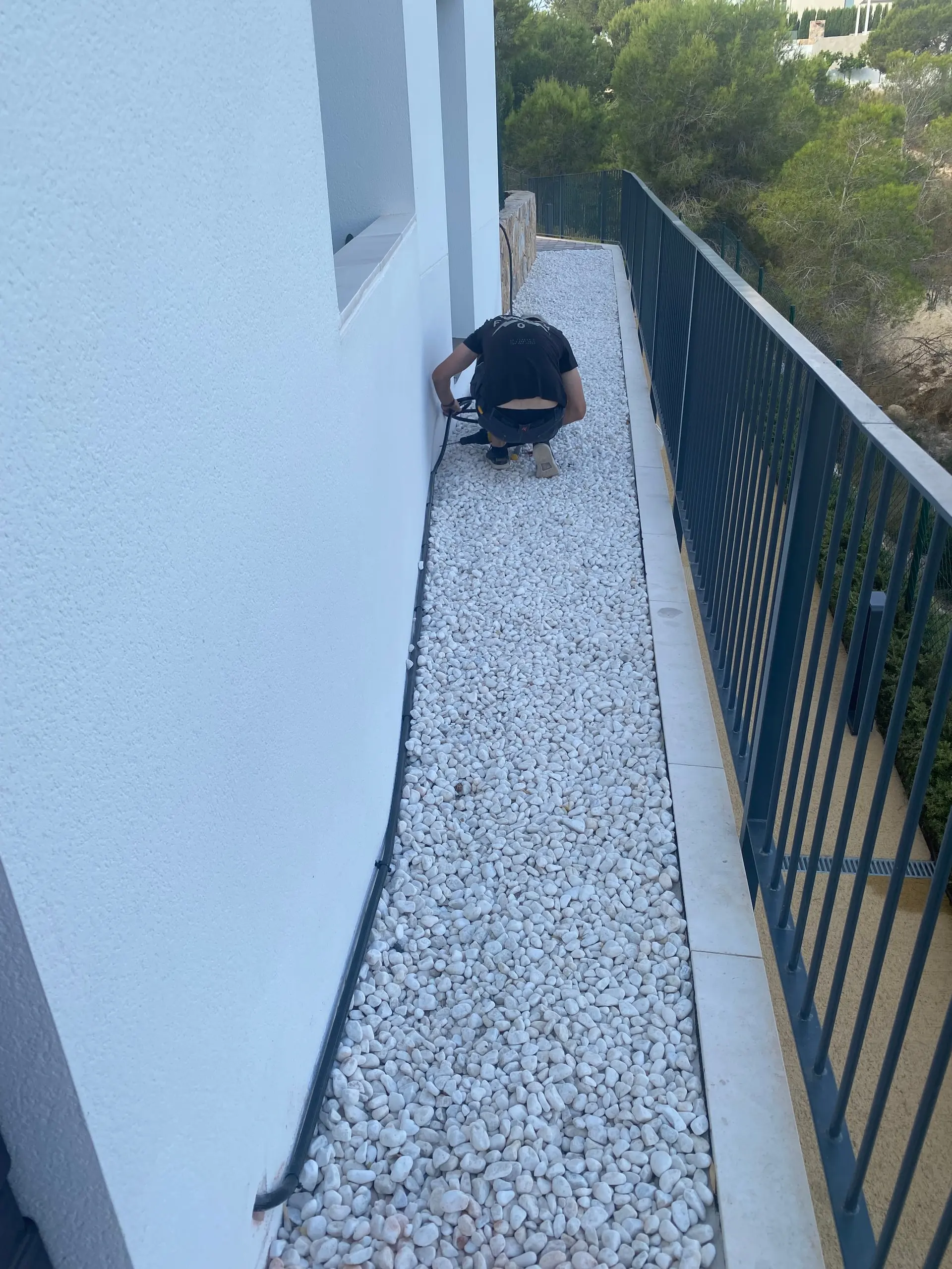 Electrician crouched running cable along a strip of white gravel between the wall and the railing