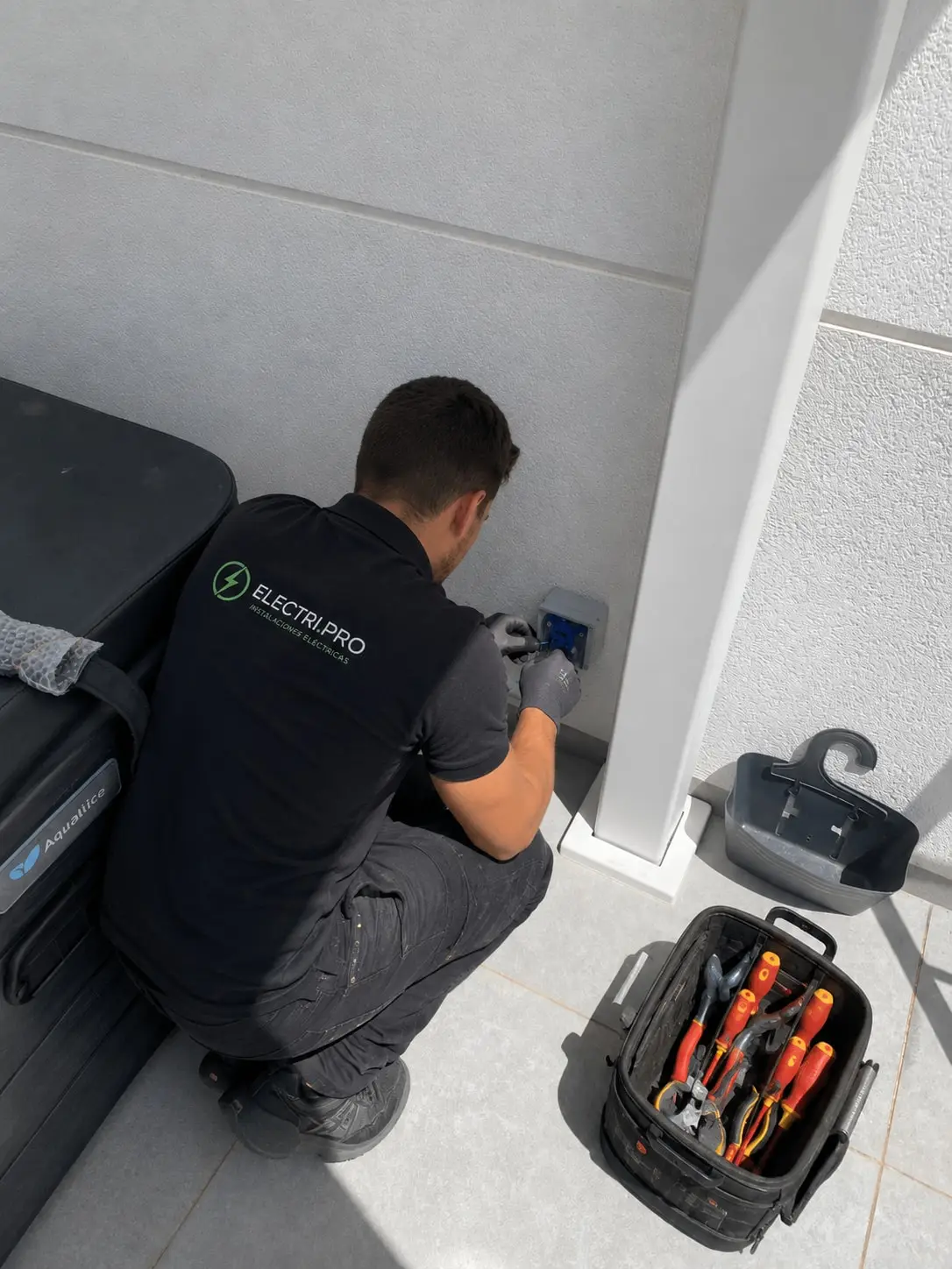Electrician making off a weatherproof box on the wall, beside the spa cover