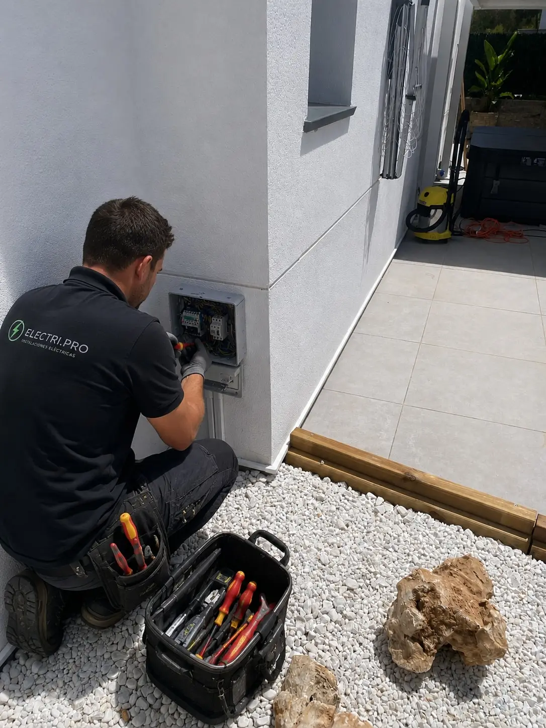 Electrician wiring DIN-rail devices inside a box recessed into the outside wall