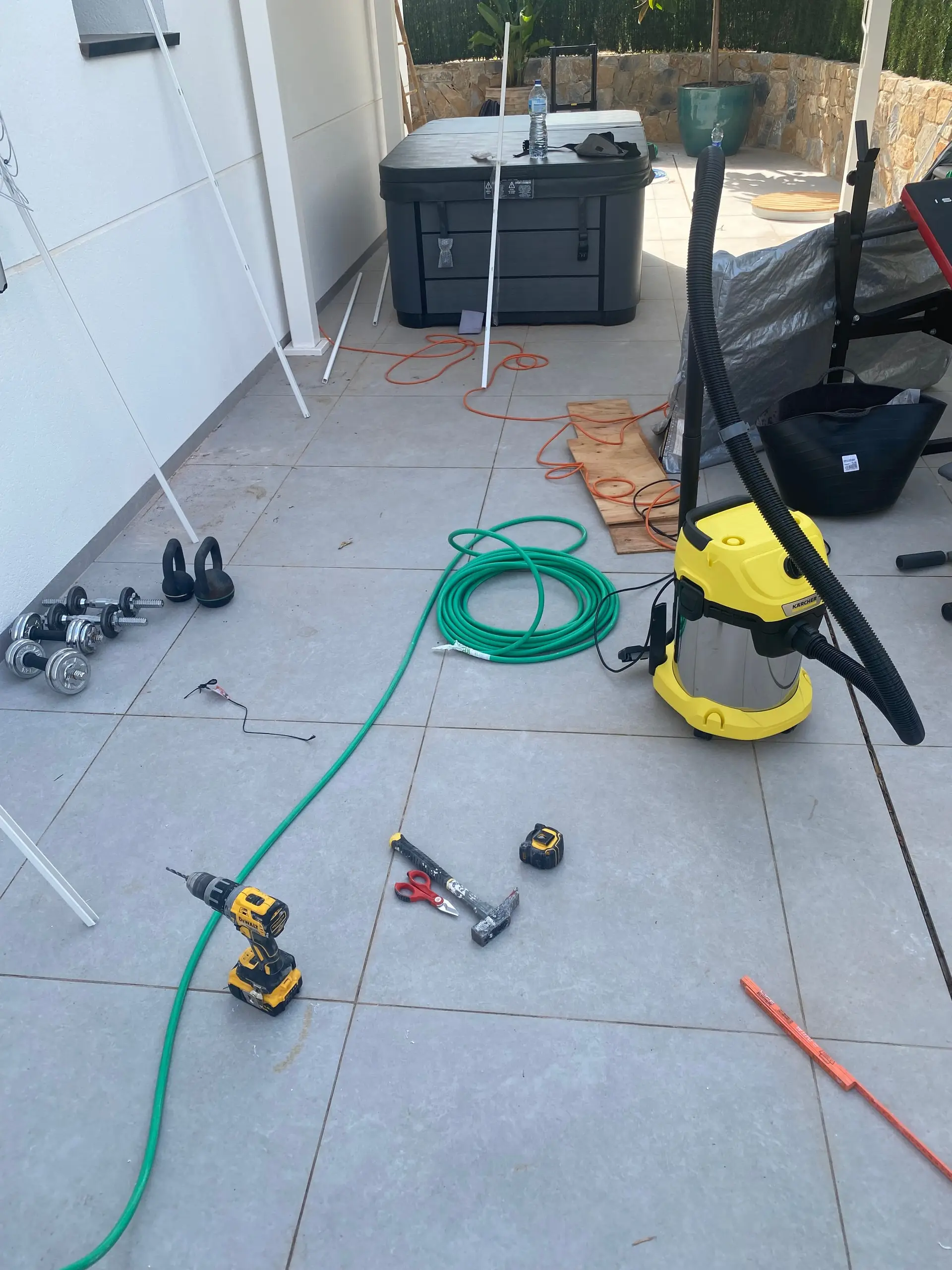 Drill, hammer and hose on a terrace floor, with the spa still crated in the background