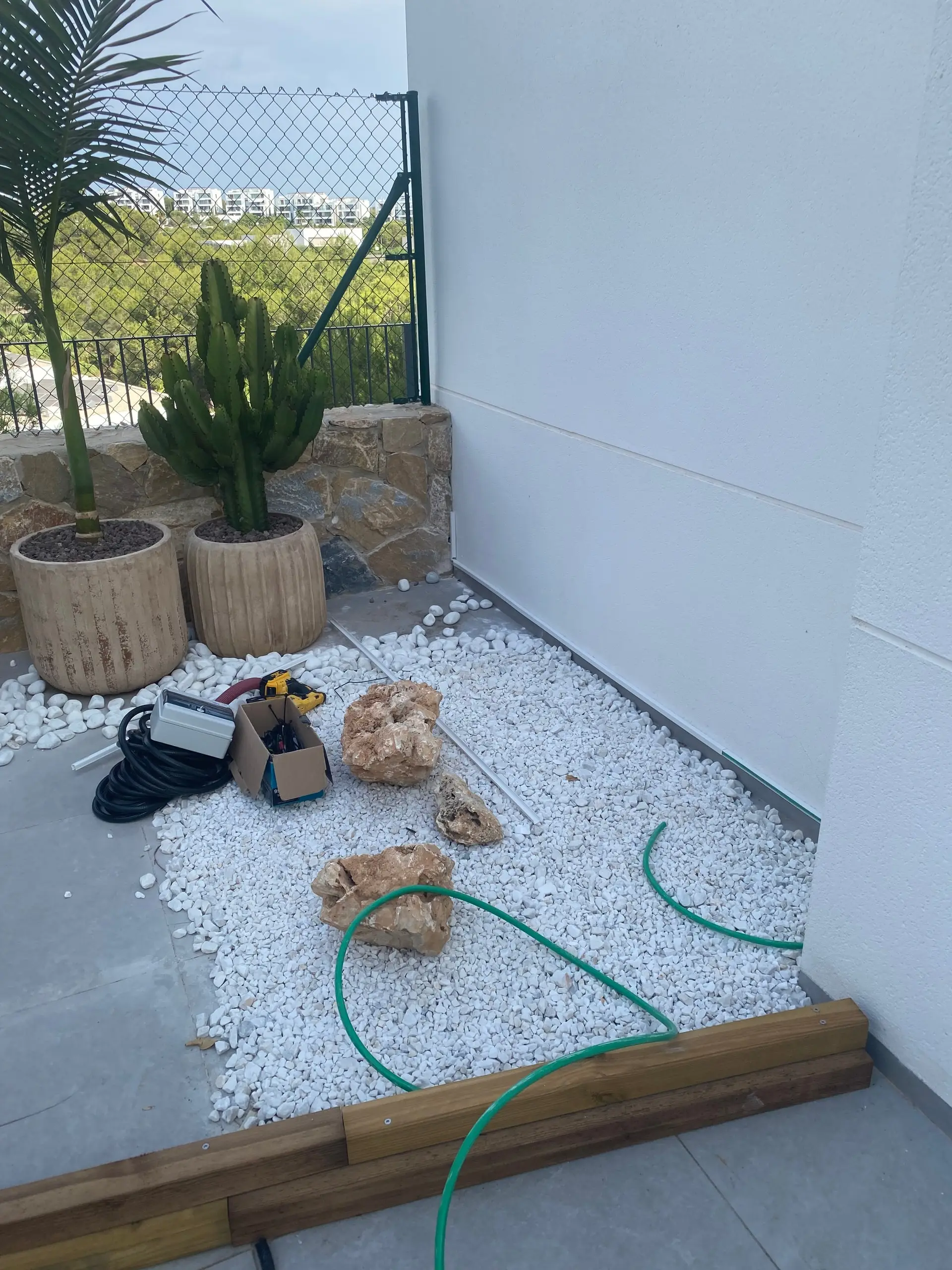 A white-gravel corner with a coil of cable and an electrical box laid out beside the planters