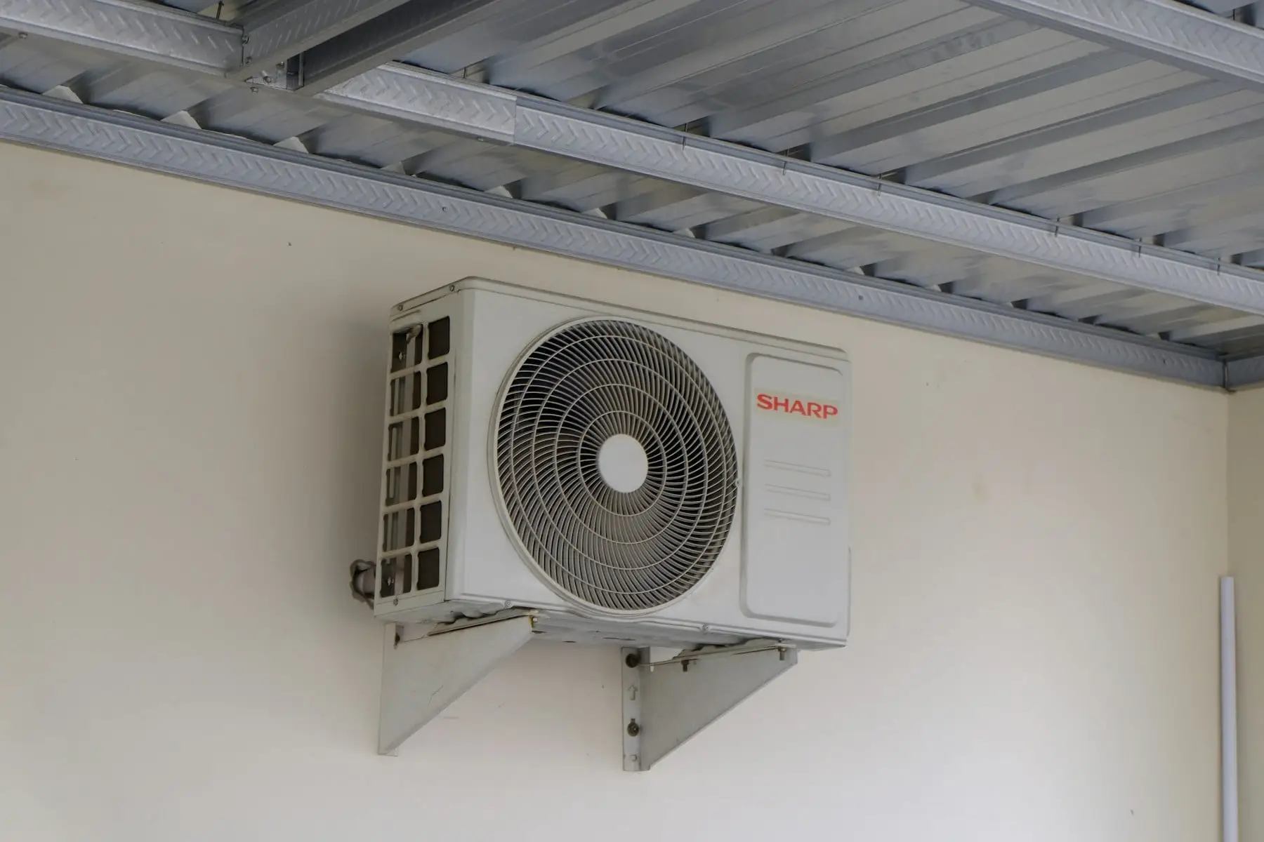 Outdoor air conditioning unit fixed to the wall on steel brackets under a metal roof
