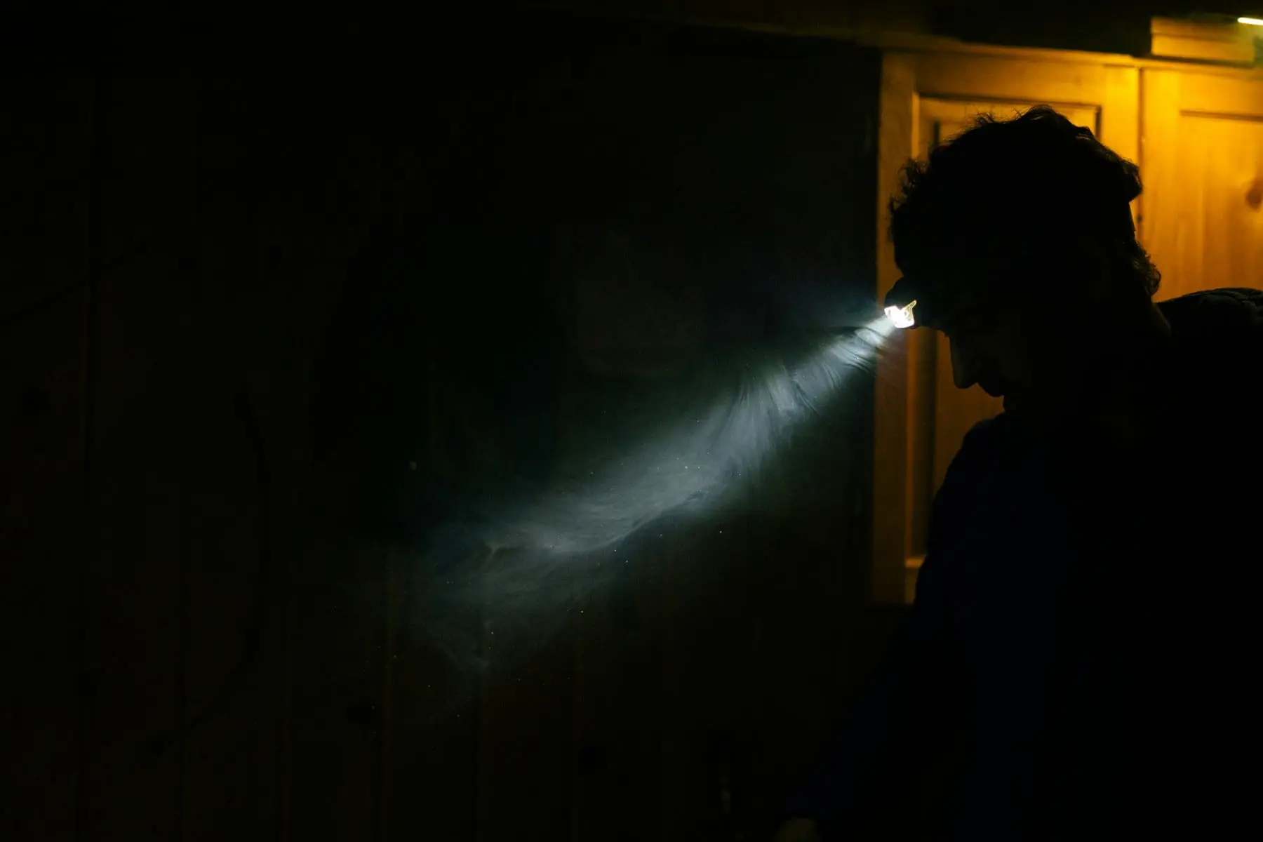 Person in a dark room lighting the wall with a head torch during a power cut