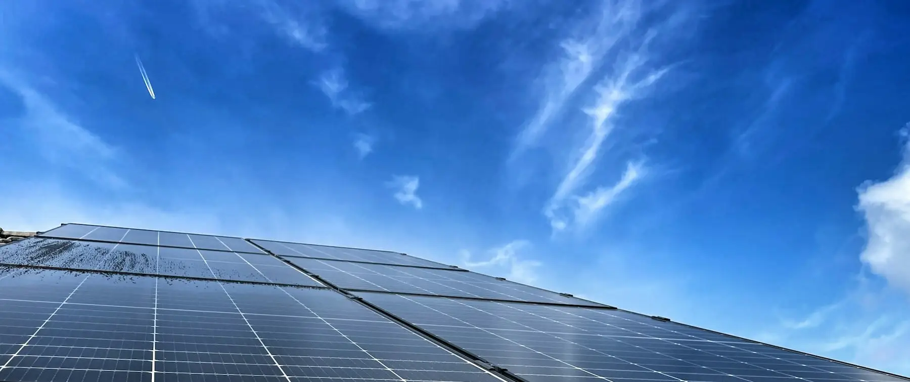 A roof of solar panels under a deep blue sky with thin high cloud