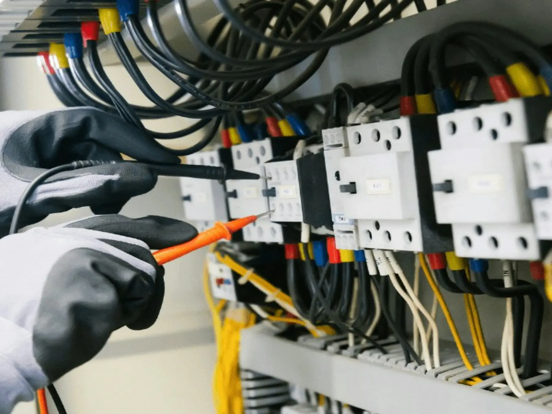 Gloved hands testing the contactors of an electrical panel with multimeter probes